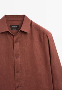 Rust-colored linen shirt with a button-down collar, featuring a textured fabric, front button closure, and a label reading "Massimo Dutti."
