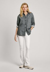 Denim overhemd met knopen in donkergrijs, met een borstzak en opgerolde mouwen, gedragen met witte flared broeken en lichte sneakers.