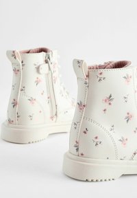 Bottes en simili cuir blanches avec un motif floral en rose et gris. Dotées d'une fermeture éclair sur le côté et d'une semelle en caoutchouc texturée pour une meilleure adhérence.