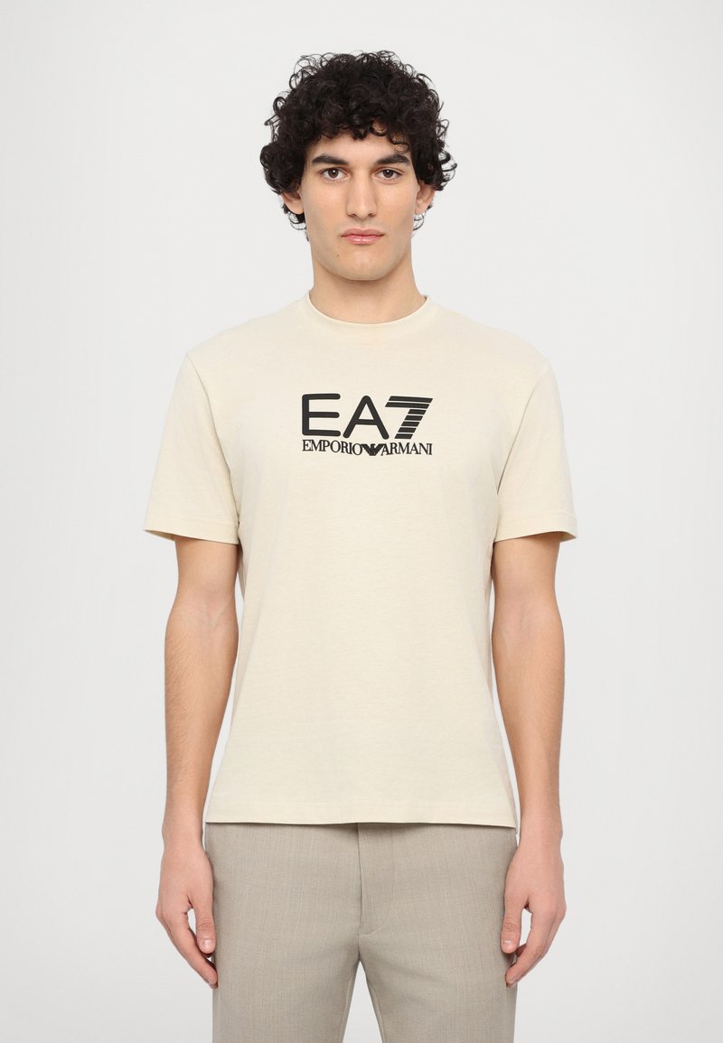 béžové bavlněné tričko s krátkým rukávem, na přední straně s černým logem EA7 Emporio Armani. Jednoduchý design s kulatým výstřihem.