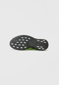 Zwarte buitenzool met witte traction-dots en groene accenten, met een gestroomlijnd ontwerp voor verbeterde grip en stabiliteit.