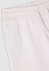 Białe spodnie dresowe z elastycznym pasem, sznurkiem do regulacji i bocznymi kieszeniami. Materiał ma subtelną diagonalną fakturę.