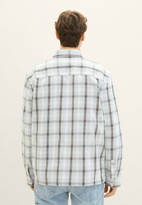 Hellblaue karierte Flanellbluse mit schwarzen und grauen Akzenten. Verfügt über einen Knopfverschluss an den Manschetten und einen abgerundeten Saum, kontrastiert durch eine glatte Textur.