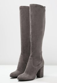 Stivali alti in suede grigio con tacco a blocco, zip laterale e texture liscia. Design elegante ideale per vari outfit e occasioni.