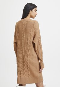 Lång beige stickad klänning med kabelstickningsdetaljer, en ribbad nederkant och avslappnad passform, med rund halsringning och sänkta axlar.