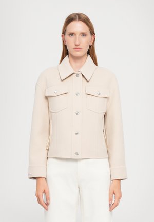 Veste cropped beige en tissu doux, dotée d'un col, de boutons argentés, de deux poches poitrine et de légers fentes sur les poignets.