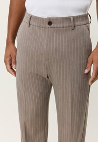 Καφέ ριγέ παντελόνια σε εφαρμοστή γραμμή, κατασκευασμένα από ελαφρύ ύφασμα, με επίπεδη μπροστινή όψη και κλείσιμο με ένα κουμπί.