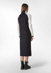 Robe en tricot noir et crème à blocs de couleur avec un col montant, des manches longues et une silhouette droite, associée à des bottes noires à lacets.