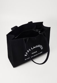 Borsa tote in tela nera con due manici, con testo stampato bianco: "KARL LAGERFELD PARIS 21 RUE ST-GUILLAUME." Apertura superiore, interno spazioso.