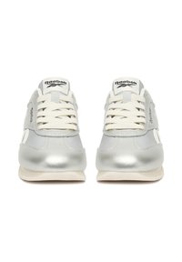 Strieborné športové tenisky s bielymi šnúrkami, textúrovaným koženým zvrškom, výrazným logom Reebok na jazyku a kontrastnými gumovými podrážkami.