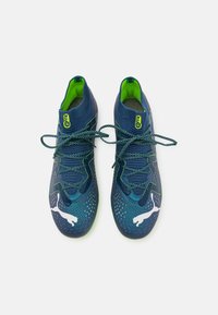 Scarpe sportive blu con tomaia texturizzata, dettagli in verde neon e design perforato. Presentano lacci e un logo bianco prominente.