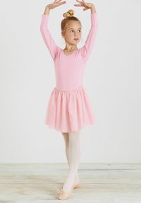 Różowy leotard z długim rękawem, z pasującą spódnicą z tiulu. Posiada dekolt w kształcie litery V, miękką fakturę i jest zestawiony z jasnoróżowymi baletkami.