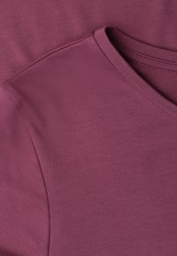 Gros plan d’un t-shirt violet à col en V montrant la texture du tissu et le détail de la couture d’épaule.