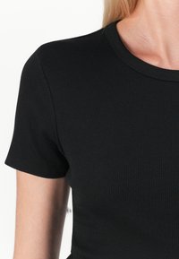 Černé žebrované tričko s kulatým výstřihem a krátkými rukávy, které má přiléhavý střih a hladkou texturu.