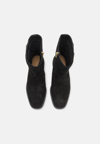 Bottes noires en velours côtelé à la cheville avec un bout carré, fermeture éclair sur le côté et détails de couture, dotées d'un intérieur lisse et de semelles plates noires.