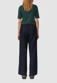 Donkerblauwe denim brede broek met hoge taille en achterzakken, gecombineerd met een aansluitend groen shirt met korte mouwen. Glad textuur.