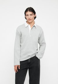 Lichtgrijze langemouwen polo met een witte kraag en een drie-knoopsluiting, gecombineerd met donkere jeans, met een ontspannen pasvorm en zachte textuur.
