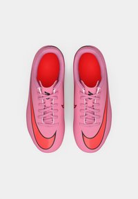 Vaaleanpunaiset urheilukengät, joissa on sileä synteettinen pinta, punainen verkkovuori, litteät vaaleanpunaiset nauhat ja suuri punainen Nike-logomerkki kummallakin sivulla.