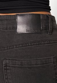 Jeans de ganga pretos com uma textura suave, apresentando um rótulo em couro na cintura que diz "Denim Project" e detalhes no bolso das costas.