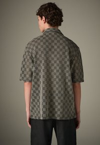 Camicia a maniche corte con motivo a zigzag nero e crema. Vestibilità rilassata con collo e tessuto testurizzato. Vista posteriore, senza grafiche visibili.