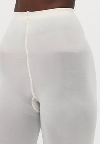 Høyt midje, gjennomsiktige hvite leggings med et teksturert mønster. Har en forsterket midje og frontkile for ekstra støtte.