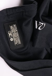 Μαύρο ύφασμα με μια ετικέτα που γράφει «ACTIVE DISCOVERY A PROGRAM BROUGHT TO YOU BY RIWHA PROJECTS» και λευκό κεντημένο κείμενο «V7» κοντά.