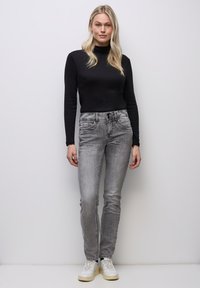 Svart tajt polotröja kombinerad med ljusgrå jeans med en lätt blekt textur och två framfickor, kompletterad med vita sneakers.