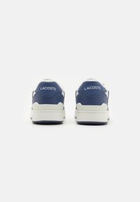 Zapatos deportivos de cuero azul marino con acentos blancos, que cuentan con un respaldo texturizado, un collar acolchado y la marca "LACOSTE" en el talón.