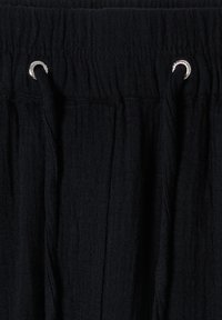 Ceinture en tissu noir avec des fronces élastiques et deux œillets métalliques argentés maintenant un cordon noir assorti, vue en gros plan.