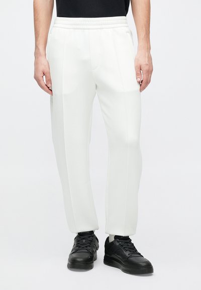 Biele zúžené tepláky s elastickým pásom. Hladká, ľahká tkanina. Kombinované s čiernymi teniskami so štruktúrovaným povrchom a polstrovaným golierom.