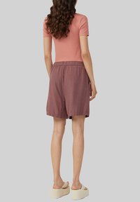 Krótke, jasnofioletowe spodenki z elastycznym paskiem w talii, zestawione z dopasowaną różową bluzką. Modelka nosi beżowe sandały na platformie.
