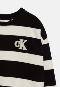 Felpa a righe bianche e nere con scollatura rotonda, dotata di un logo "cK" bianco testurizzato nella zona del petto. Tessuto morbido.