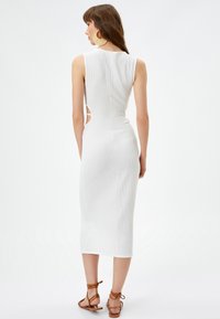 Witte, geribbelde midi-jurk met een getailleerde silhouet, open zijuitsparingen en zonder mouwen. Gepaird met bruine sandaaltjes met bandjes.