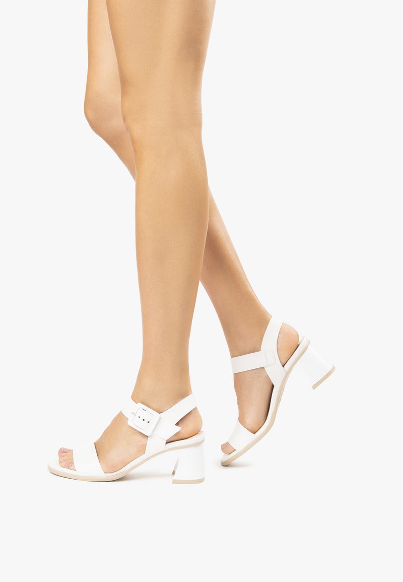 Sandales à talons blancs avec une bride à boucle, bout ouvert et talon épais. Matériau lisse avec un design minimaliste et bride de cheville réglable.