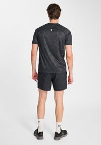 Czarna koszulka sportowa z teksturowanym, wzorzystym materiałem; w komplecie z pasującymi szortami. Posiada krótkie rękawy oraz logo na plecach.