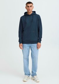 Sudadera azul marino con un bolsillo delantero, capucha con cordón y dobladillo acanalado. Combinada con jeans de color azul claro y zapatillas blancas. Textura suave.