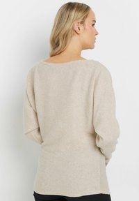 Beige ribbade sweater med lös passform och vid halsringning, med långa ärmar och en något förlängd bakslits.