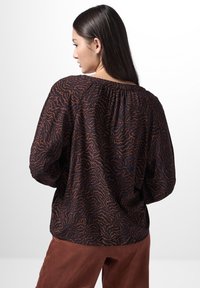 Dunkel gemusterte Bluse mit langen Ärmeln, die ein strukturiertes, gewelltes Design in Rost- und Marineblau-Tönen sowie einen gerafften Ausschnitt aufweist.