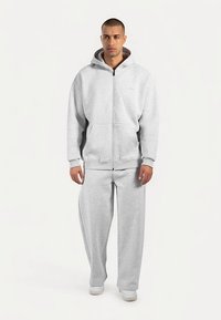 Felpa grigia con zip, cappuccio, tasche frontali e pantaloni della tuta abbinati. Realizzata in tessuto morbido, con vestibilità comoda e polsini elasticizzati.