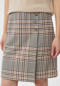Geruite rok met bruine, crème en zwarte patronen. Voorzien van een knoopsluiting en een subtiele plooidetail. Gemaakt van textuurstof.