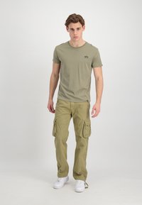 Olive green crew-neck t-shirt paired with matching cargo pants. Pants feature large side pockets and drawstring hem, complemented by white sneakers.