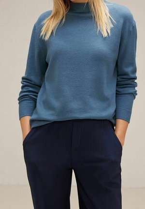 Pullover strutturato azzurro chiaro con colletto alto, abbinato a pantaloni a coste blu navy. Entrambi i capi presentano una vestibilità rilassata e tasche laterali.