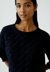 Marineblaue Strickjacke mit einem strukturierten Wellenmuster, geripptem Kragen und Dreiviertelärmeln. Weicher Stoff, lässiges Design.