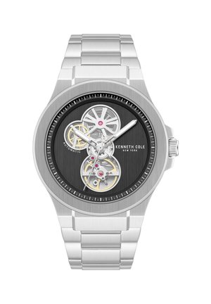 Orologio da polso con cinturino in metallo argentato e quadrante nero che mostra ingranaggi meccanici argentati e dorati esposti, lancette bianche che indicano le 10:09:37.