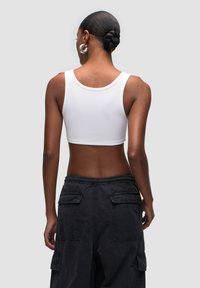 Top corto bianco a costine con spalline larghe, abbinato a pantaloni cargo neri con tasche laterali e vita elastica.