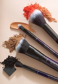 Set aus vier Make-up-Pinseln mit schwarzen Griffen, lila Akzenten und weichen Borsten. Enthält Kosmetika in orange, braun und schwarz.