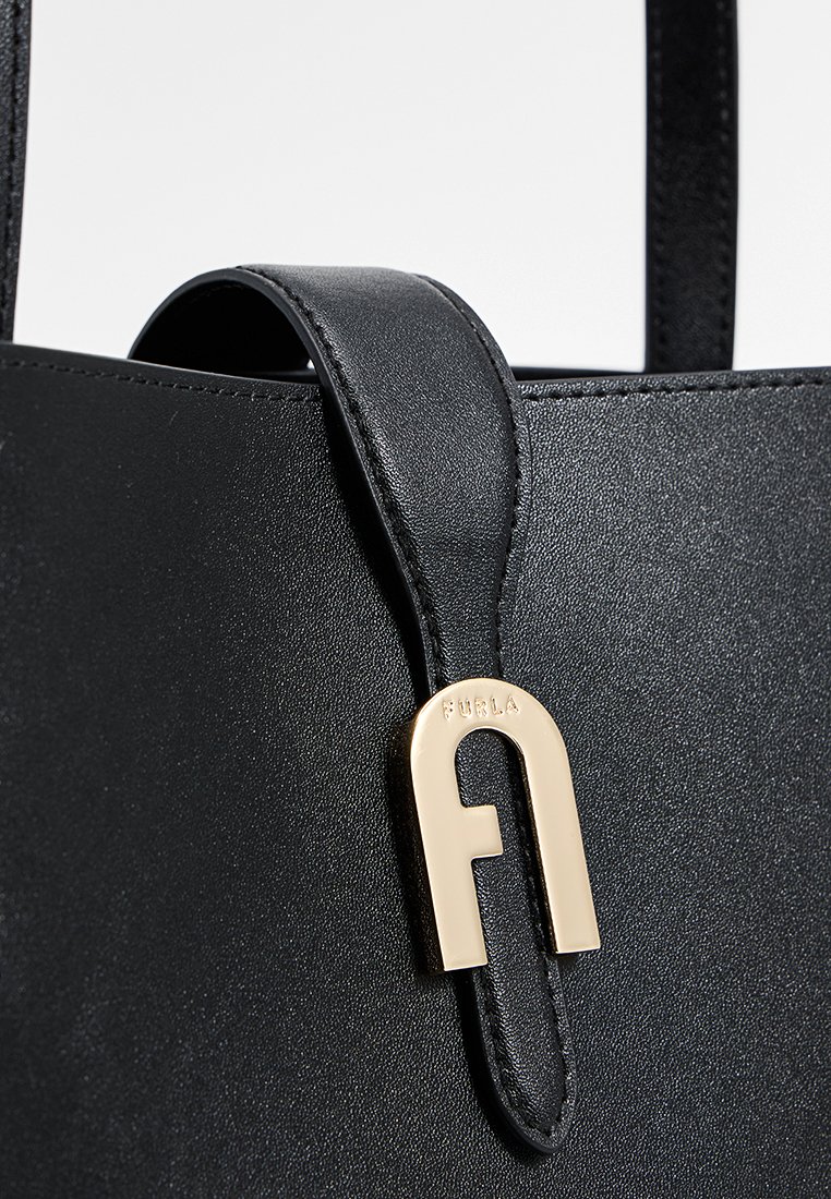 Sac fourre-tout en cuir noir avec une texture lisse, un clip en métal doré proéminent et un logo en relief sur le clip.