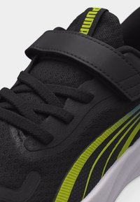 Μαύρο αθλητικό παπούτσι με υφασμάτινη υφή, μαύρα κορδόνια, φαρδιά λουρίδα και λεπτομέρεια σε νέον πράσινη ρίγα κατά μήκος της πλευράς.