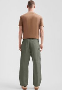 Brązowy t-shirt z krótkim rękawem połączony z luźnymi oliwkowymi spodniami z kieszeniami cargo i subtelną teksturą. Obuwie ma jasnobrązowy odcień.