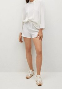 Witte geribbelde hoodie met een voorzak, gedragen met bijpassende witte shorts. De outfit wordt aangevuld met beige en witte sneakers.